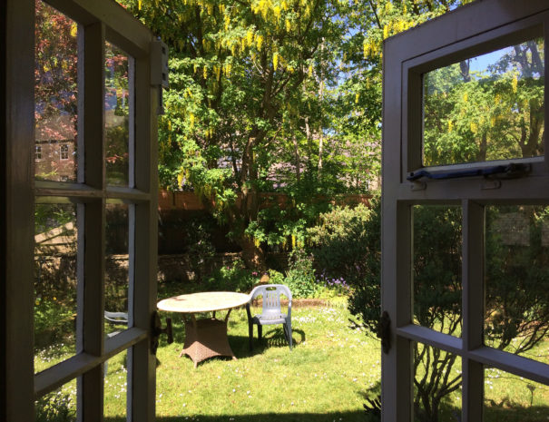 View of a sunny walled garden with table and chair through open French windows
